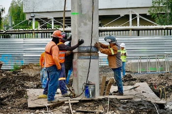 Trabajadores con cascos y chalecos de seguridad ajustan una columna de concreto en un terreno en construcción