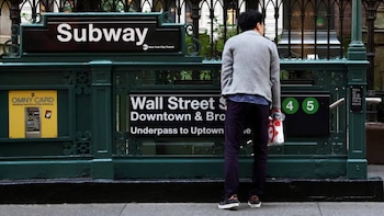 Un hombre de espaldas se para frente a una entrada de metro verde ornamentada con letreros que indican "Subway" y "Wall Street", líneas 4 y 5, en Nueva York