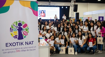 Banner con logo de EXOTIK NAT, grupo de niñas y adolescentes con certificados y bolsas. Al fondo, un escenario con pantalla y presentadoras en un evento.