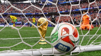 Portería de fútbol con balón en la red, copa del Mundo dorada, jugadores y portero en cancha de césped, gradas llenas de aficionados en estadio de Los Ángeles.