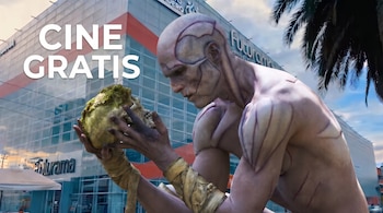 Figura de una criatura humanoide con vendajes que sostiene un cráneo frente a un edificio urbano, con las palabras Cine gratis en letras blancas.