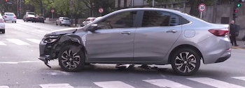 Automóvil sedán gris con daños en el guardabarros delantero y restos en el asfalto junto a un paso peatonal