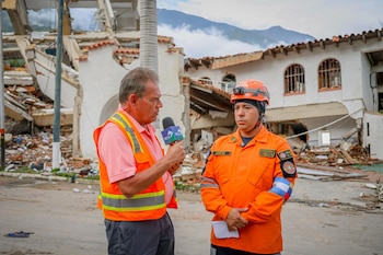 El periodista Moisés Urbina entrevista a un integrante del equipo de búsqueda y rescate salvadoreño frente a una estructura colapsada en Venezuela, durante la cobertura de las operaciones tras los terremotos (Cortesía Secretaría de Prensa).
