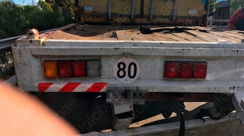 Parte posterior de un remolque de camión blanco con un cartel circular de velocidad de 80, luces traseras y una matrícula pixelada.