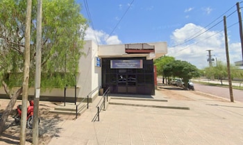 Fachada de una comisaría de policía con rampa de acceso, árboles y postes de luz sobre la vereda