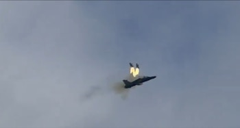 Un avión militar de color oscuro vuela mientras dos asientos con estelas de fuego se proyectan hacia arriba