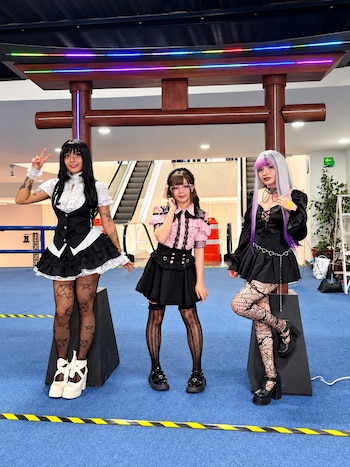 Tres mujeres con vestidos de estética japonesa posan de pie junto a un arco torii de madera en un recinto de eventos