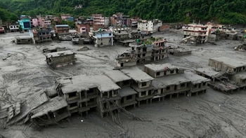 Vista aérea de varias casas sepultadas parcialmente por una capa de lodo gris junto a una montaña verde