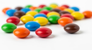 Varios caramelos de colores brillantes tipo M&M’s sobre una superficie blanca en primer plano