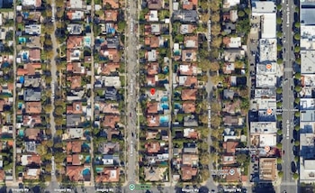 Vista aérea satelital de una cuadrícula urbana con casas, piscinas, calles arboladas y un marcador rojo sobre una residencia