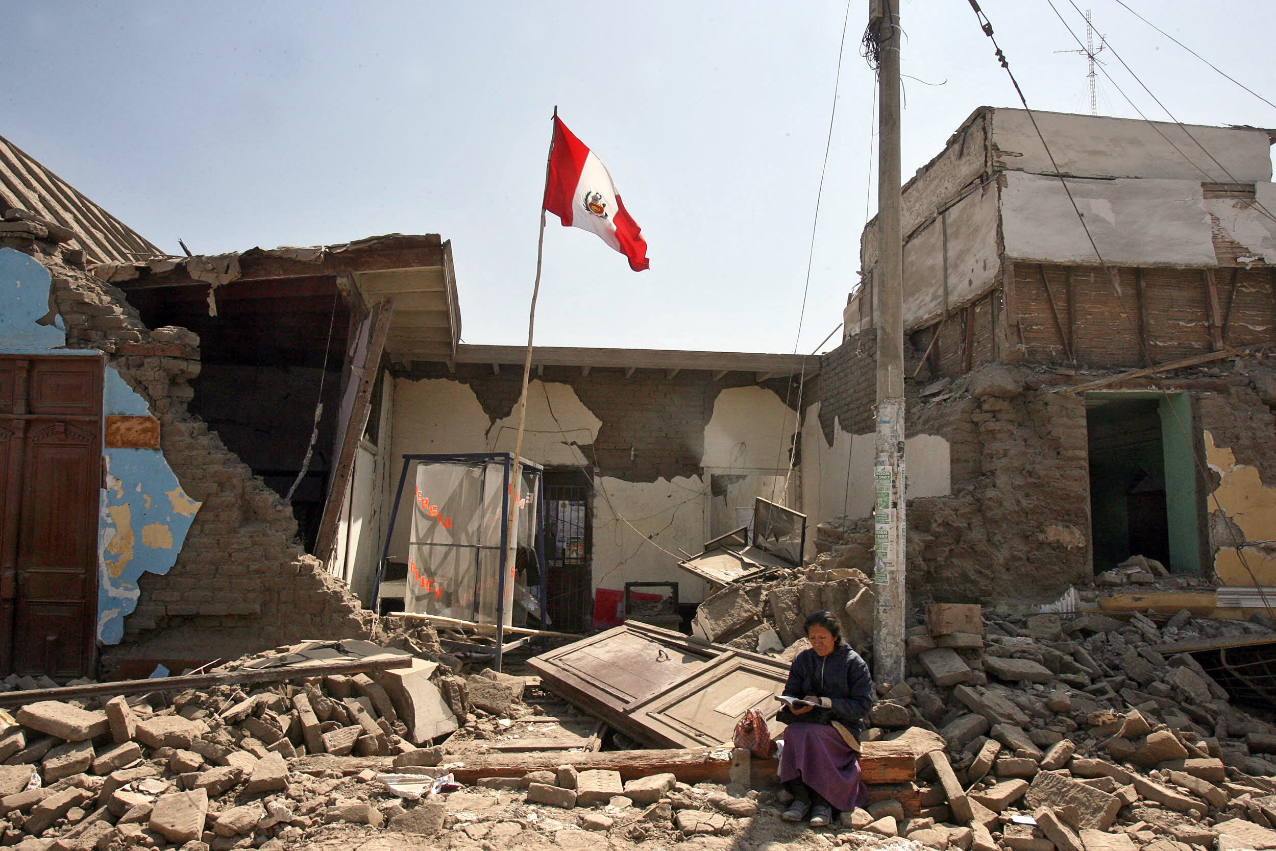 A woman reads the bible in front of her destroyed house in Pisco, more than 300 km south of Lima, 16 August 2007. Peruvian officials struggled on Thursday to reach cut-off victims on the country