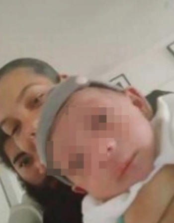 Primer plano de una mujer con un bebé en brazos; una segunda persona se ve parcialmente al fondo; el rostro del bebé está pixelado
