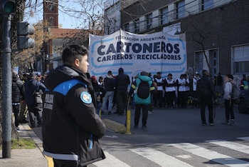 Agente de policía en primer plano. Detrás, pancarta de Federación Argentina Cartoneros, Carreros y Recicladores, personas congregadas y edificios en calle