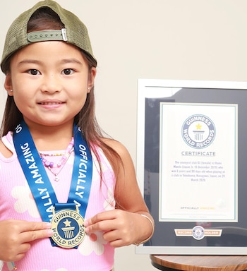 Una niña con gorra verde sostiene una medalla en su pecho junto a un certificado enmarcado sobre una mesa