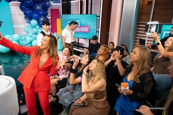 Grupo de personas sonriendo y fotografiando con teléfonos móviles en un estudio de televisión; globos azules y una pantalla con '¡Siéntese quien pueda!' al fondo