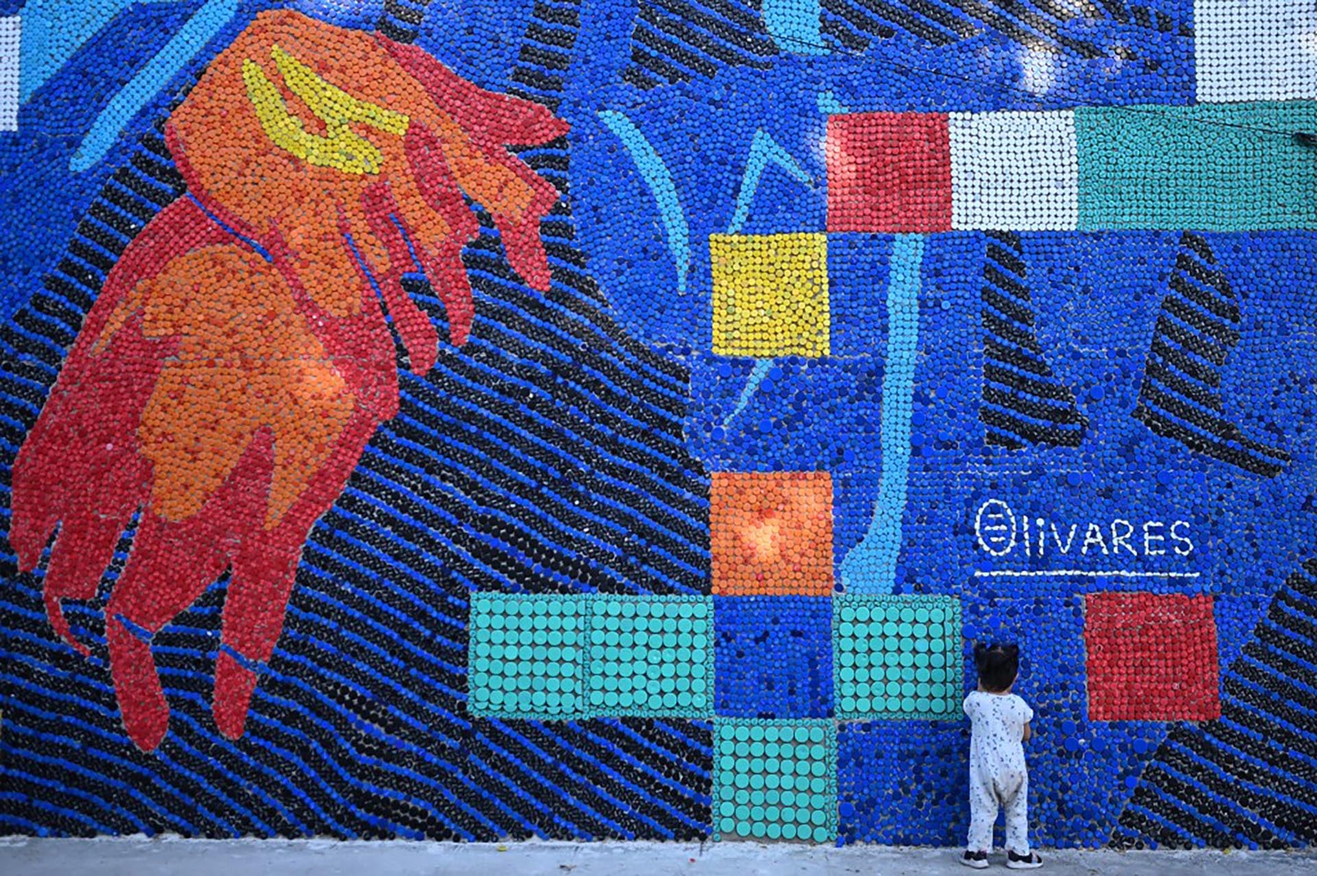 Una niña observa el impresionante mural 'Mona Lisa latinoamericana', creado por el artista Olivares utilizando miles de tapas de botellas de plástico recicladas, fusionando arte y conciencia ambiental.