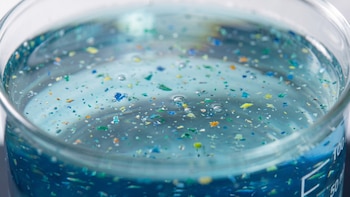 Primer plano de un recipiente de vidrio con líquido transparente que contiene partículas diminutas de varios colores y burbujas