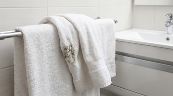 Toalla de baño blanca con una mancha oscura de moho, colgada en un toallero cromado dentro de un baño con azulejos blancos y un lavabo.