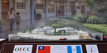 Maqueta a escala de un complejo de edificios bajo una cubierta transparente, sobre una base con las banderas de Taiwán y Guatemala