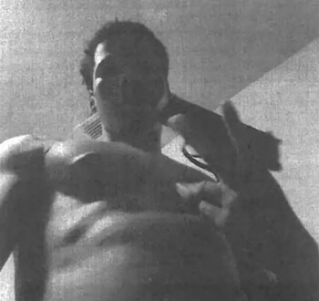 Fotografía en blanco y negro desde un ángulo bajo de un hombre sin camiseta que sostiene una pistola