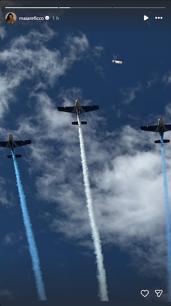 Cielo azul con nubes blancas dispersas y tres aviones ascendiendo, dejando estelas de humo blanco y azul, con un cigarrillo encendido flotando en la parte superior