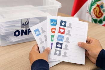Manos sostienen tres cédulas de votación impresas con símbolos sobre una mesa, junto a una urna con la marca ONPE y la bandera de Perú.