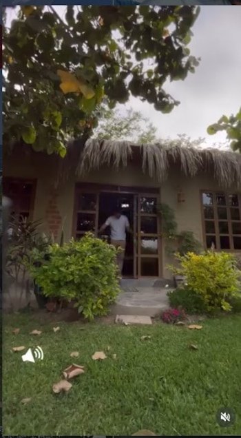 Óscar López Arias saliendo de una casa de campo con techo de paja. Hay césped verde y arbustos alrededor de la entrada