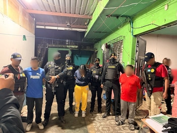 Varios agentes policiales con chalecos tácticos y armas custodian a tres personas con rostro difuminado dentro de un inmueble