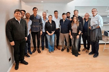 Grupo de once personas, incluyendo hombres y dos mujeres, posan de pie y sonriendo en una habitación moderna con paredes blancas y suelo de madera clara