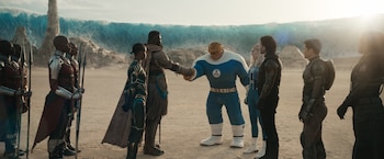 Winston Duke como M'Baku estrechando la mano de La Mole, rodeados por guerreras Dora Milaje y otros héroes en un paisaje desértico con una ola gigante al fondo