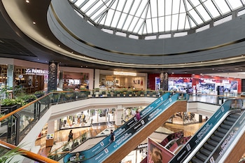 Interior multinivel del centro comercial Unicenter con escaleras mecánicas, barandales de vidrio, personas, tiendas y una cúpula de cristal en el techo