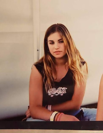 Retrato de una joven con cabello largo y rubio cobrizo, camiseta negra sin mangas con un gráfico y pulseras en la muñeca derecha, mirando al frente