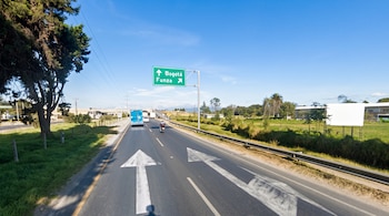 Carretera asfaltada con flechas pintadas en el suelo, un letrero verde con indicaciones hacia Bogotá y Funza, vehículos y árboles