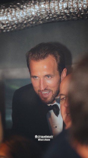 Harry Kane sonríe vestido con esmoquin negro y pajarita junto a otra persona en un entorno con iluminación tenue