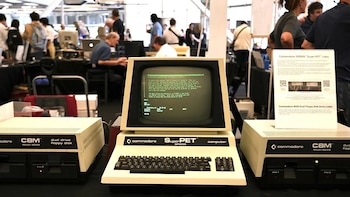Computadora Commodore Super PET SP9000 con monitor verde, teclado y dos unidades de disquete. Un cartel con texto está a la derecha