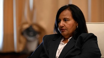 Retrato en plano medio de Dinorah Figuera vestida con saco oscuro y camisa blanca frente a un fondo beige
