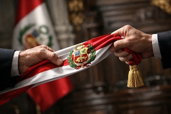 Primer plano de dos manos sujetando una banda presidencial peruana roja y blanca con el escudo nacional bordado, sobre un fondo desenfocado de una bandera y arquitectura.