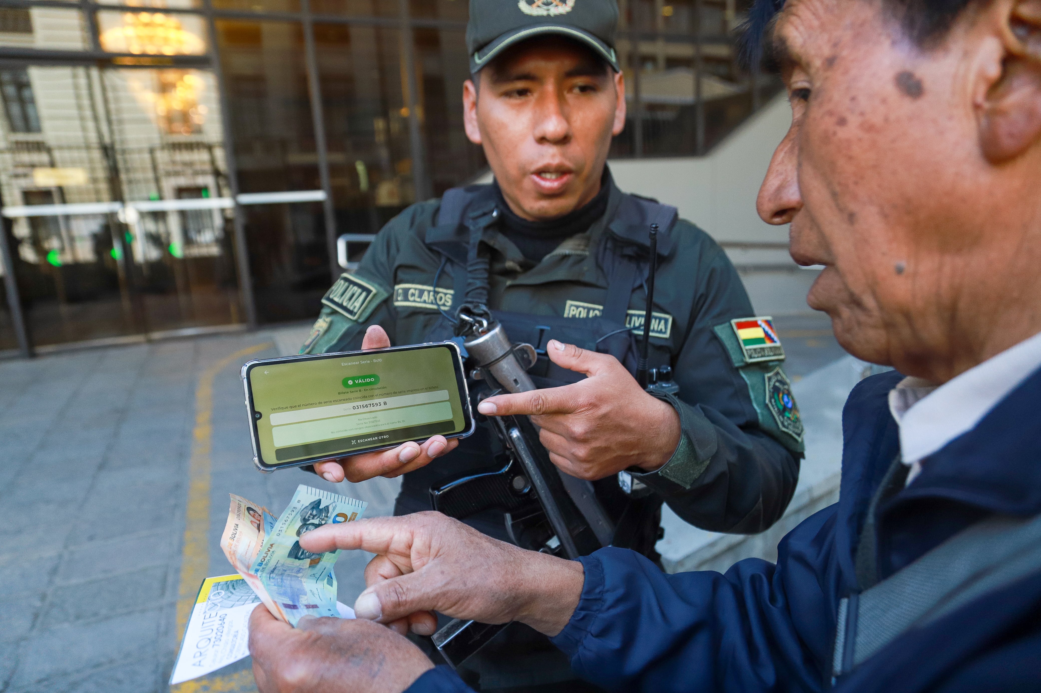 Un integrante de la Policía de Bolivia (i) revisa billetes de la serie B a un ciudadano en la sede del Banco Central de Bolivia (BCB) este miércoles, en La Paz (Bolivia). EFE/ Gabriel Márquez