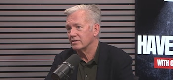 Chris Hansen habla frente a un micrófono negro en un estudio con una pared de franjas horizontales