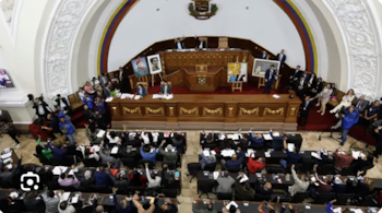 Vista elevada del hemiciclo de un parlamento con diputados levantando la mano en sus escaños y cuadros al frente del recinto