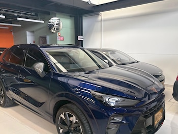 SUV azul oscuro, automóvil gris, espejo convexo, señales de tráfico, licencia colombiana, techo con iluminación, pared clara y piso de baldosas