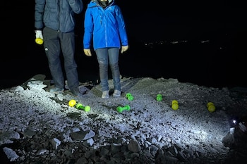 Dos personas vestidas con chaquetas de abrigo permanecen de pie de noche sobre piedras junto a varias mancuernas de colores