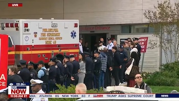 Varios oficiales de policía y personas se encuentran junto a una ambulancia frente a la entrada de urgencias de un centro de salud