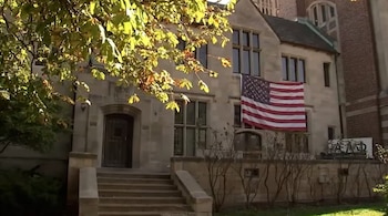 Fachada de un edificio de piedra con escalones de acceso, una bandera de Estados Unidos colgada de una ventana y las letras griegas Alpha Delta Phi