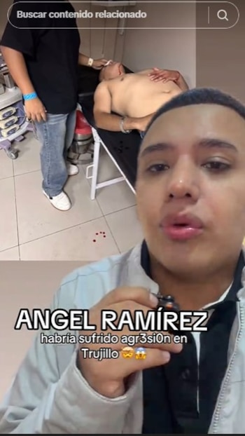 Un hombre sin camisa yace en una camilla mientras otro lo asiste; gotas de sangre se ven en el suelo. En primer plano, el rostro de un hombre hablando a cámara