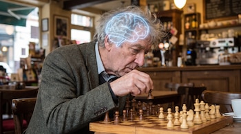 Hombre de cabello gris mueve pieza de ajedrez en tablero de madera. Su cerebro se muestra en color azul brillante. Fondo de cafetería con barra y estantes.
