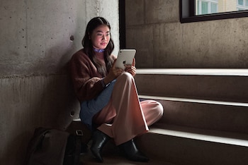 Una mujer sentada en unos escalones de concreto sostiene con ambas manos una tableta gris con el logotipo de Apple