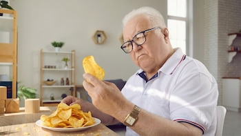 Hombre mayor examina una papa frita con expresión pensativa - VisualesIA ScribNews