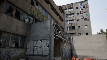 Fachada de dos edificios de concreto con grafitis y numerosas ventanas rotas o faltantes. El edificio más alto tiene las letras NIES pintadas verticalmente