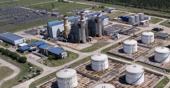 Vista aérea de una central termoeléctrica con tanques de almacenamiento de combustible, chimeneas y una subestación eléctrica